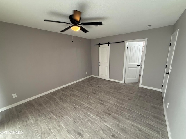 unfurnished bedroom with ceiling fan, hardwood / wood-style floors, and a barn door