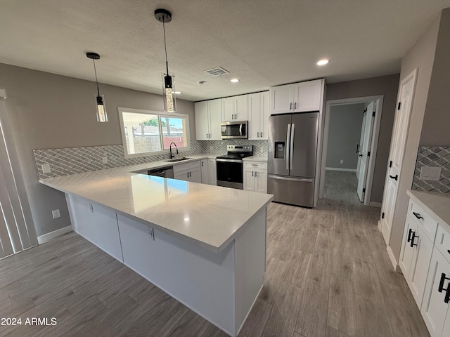 kitchen featuring stainless steel appliances, kitchen peninsula, white cabinets, and decorative light fixtures