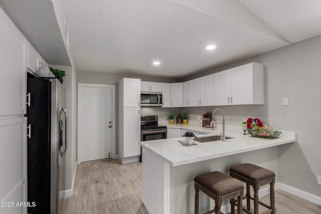 8720 W Willowbrook Dr, Peoria, AZ 85382 - kitchen featuring stainless steel appliances, a peninsula, light wood finished floors, a breakfast bar area, and white cabinetry