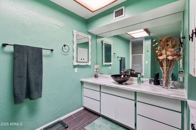 bathroom featuring visible vents, vanity, baseboards, and a textured wall