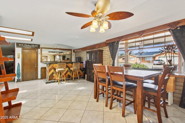 dining room with light tile patterned floors, a bar, a ceiling fan, and vaulted ceiling