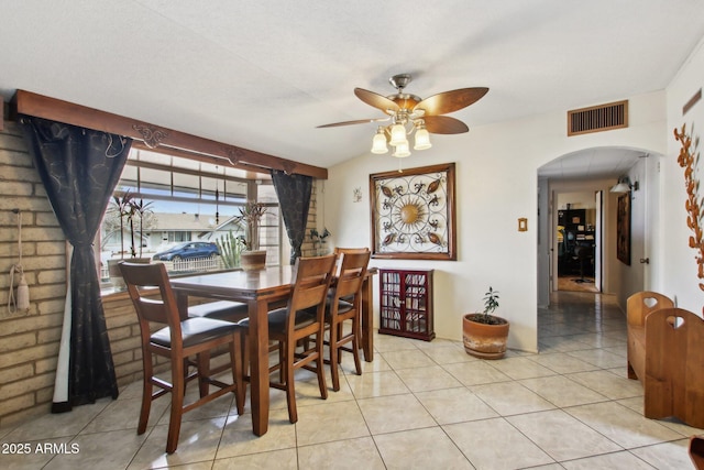 dining space with light tile patterned floors, a ceiling fan, visible vents, and arched walkways