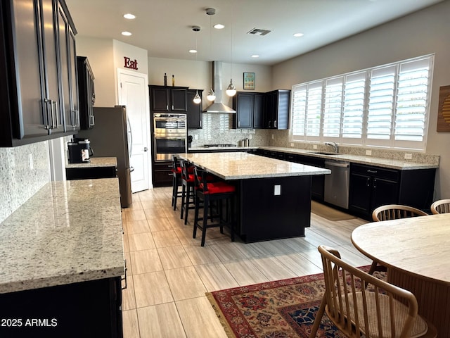 kitchen with pendant lighting, appliances with stainless steel finishes, extractor fan, light stone countertops, and a kitchen island