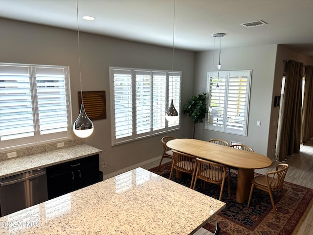 kitchen with hanging light fixtures, dark hardwood / wood-style floors, stainless steel dishwasher, and light stone counters