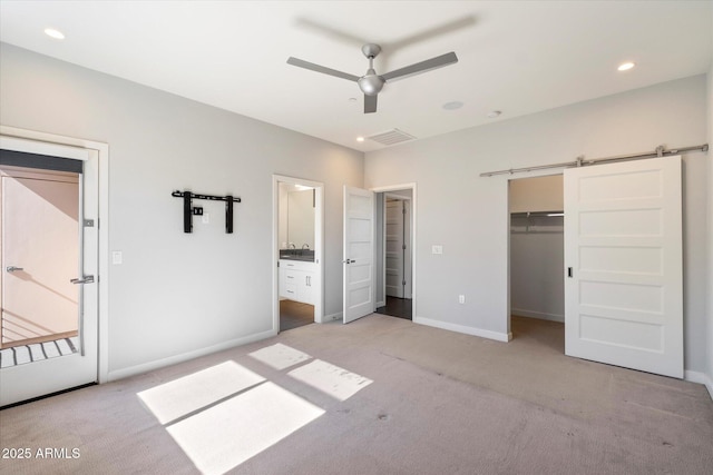 unfurnished bedroom featuring ensuite bath, a barn door, a walk in closet, light colored carpet, and a closet