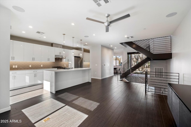 kitchen featuring high end fridge, white cabinetry, decorative backsplash, a center island with sink, and decorative light fixtures