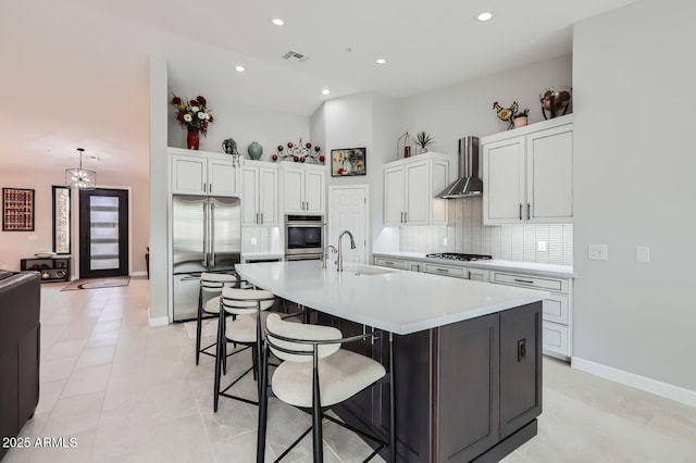 kitchen with visible vents, a sink, stainless steel appliances, white cabinets, and wall chimney range hood