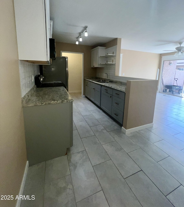 kitchen with decorative backsplash, ceiling fan, freestanding refrigerator, open shelves, and a sink