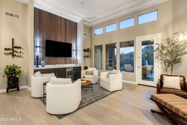 living room with light wood-style flooring, wet bar, visible vents, and baseboards