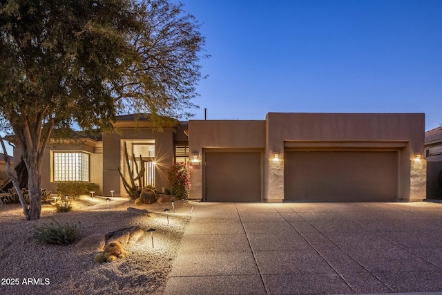 pueblo-style house with a garage, driveway, and stucco siding