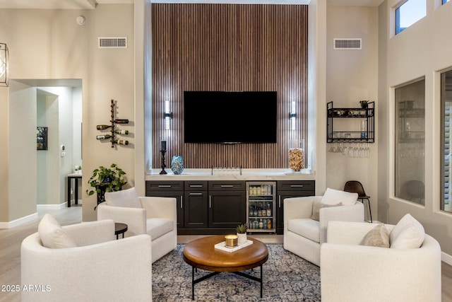 living room with baseboards, beverage cooler, visible vents, and wet bar