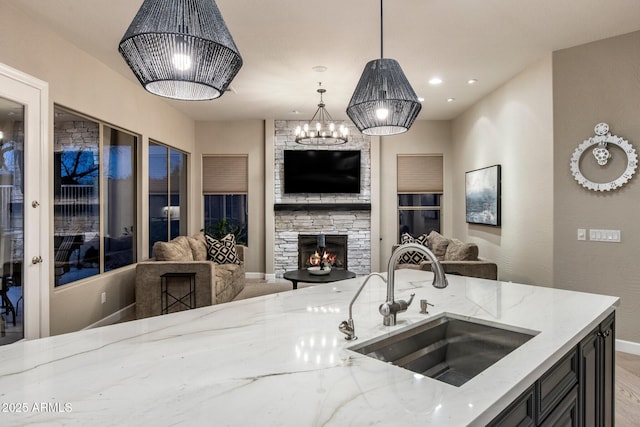 kitchen featuring light stone counters, open floor plan, hanging light fixtures, a stone fireplace, and a sink