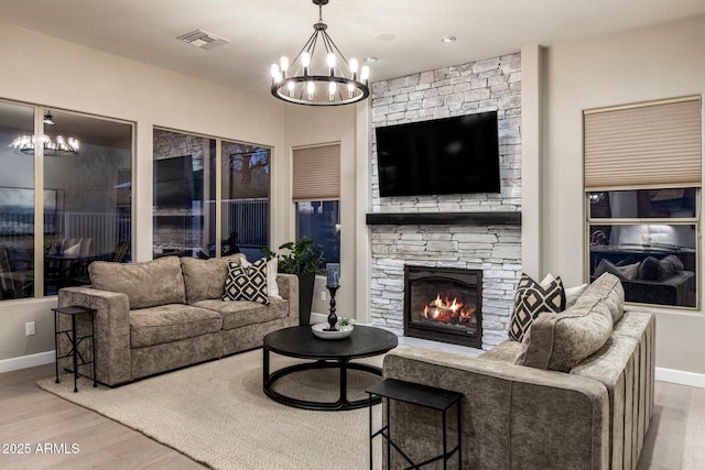 living area featuring a stone fireplace, wood finished floors, visible vents, baseboards, and an inviting chandelier