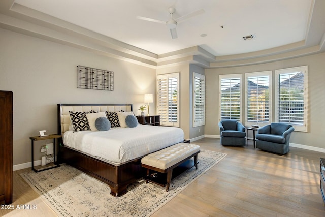 bedroom featuring wood finished floors, a raised ceiling, visible vents, and multiple windows