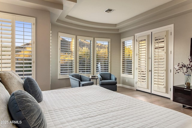 bedroom with a tray ceiling, wood finished floors, visible vents, and baseboards