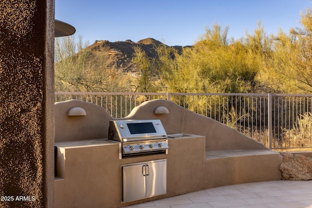 view of patio / terrace featuring exterior kitchen, a mountain view, a grill, and fence