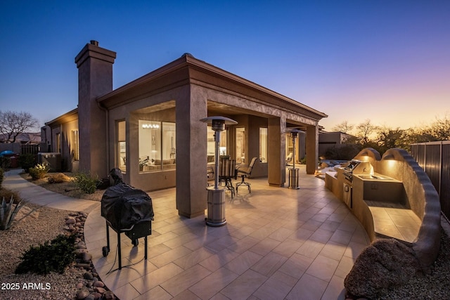 patio terrace at dusk with area for grilling, fence, and a grill