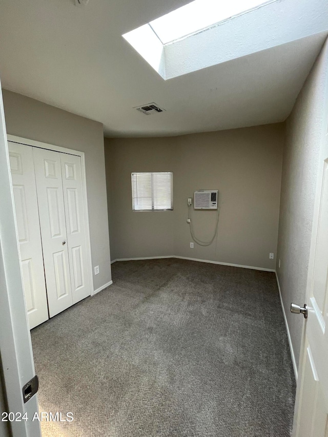 unfurnished bedroom featuring a skylight, an AC wall unit, a closet, and carpet floors