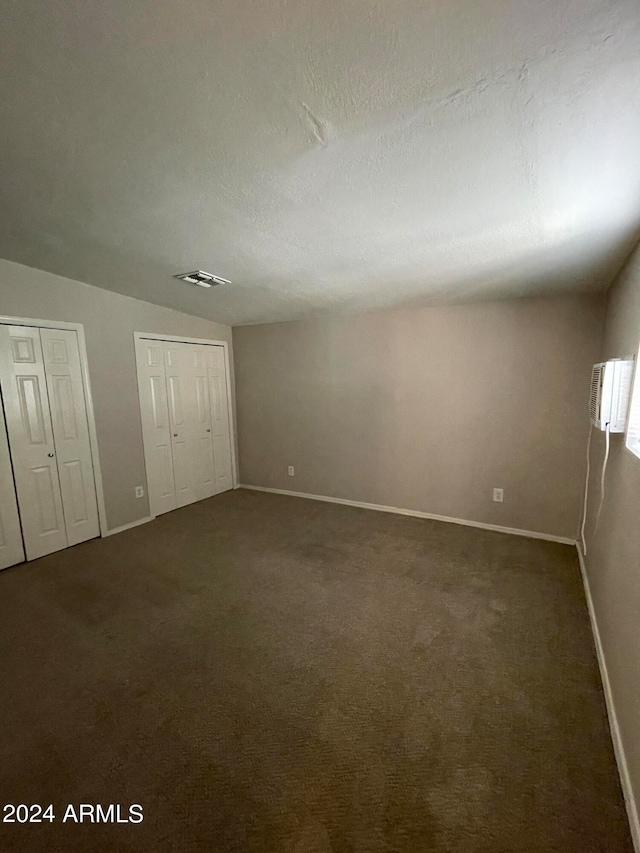 unfurnished bedroom with two closets, dark carpet, and a textured ceiling