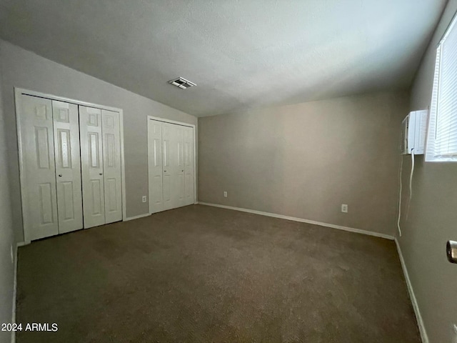 unfurnished bedroom with multiple closets, dark colored carpet, and vaulted ceiling