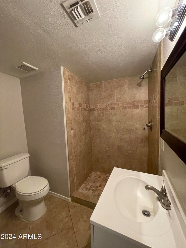 bathroom with toilet, tile flooring, a textured ceiling, vanity, and tiled shower