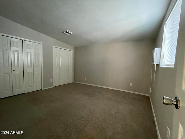 unfurnished bedroom featuring lofted ceiling, dark colored carpet, and two closets