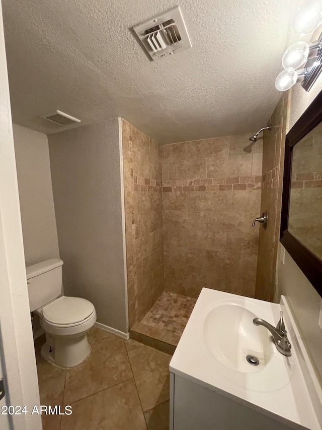 bathroom featuring toilet, a textured ceiling, vanity, tiled shower, and tile floors