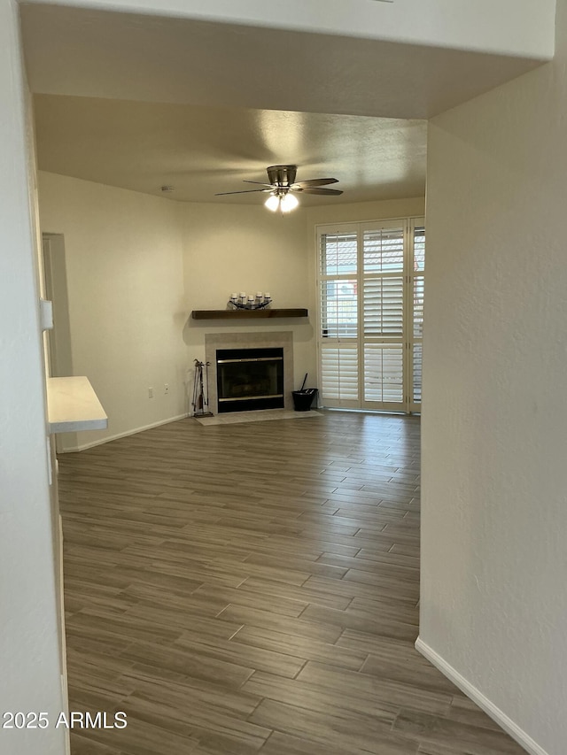 unfurnished living room featuring a fireplace with flush hearth, baseboards, ceiling fan, and wood finished floors