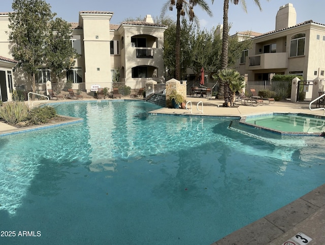 pool with fence, an outdoor fireplace, a community hot tub, and a patio