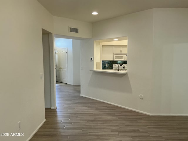 hallway featuring visible vents, baseboards, wood finished floors, a sink, and recessed lighting