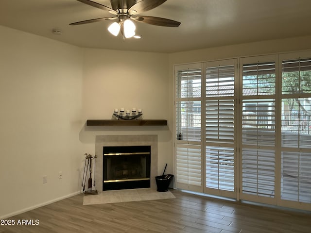 unfurnished living room featuring a ceiling fan, a tile fireplace, baseboards, and wood finished floors