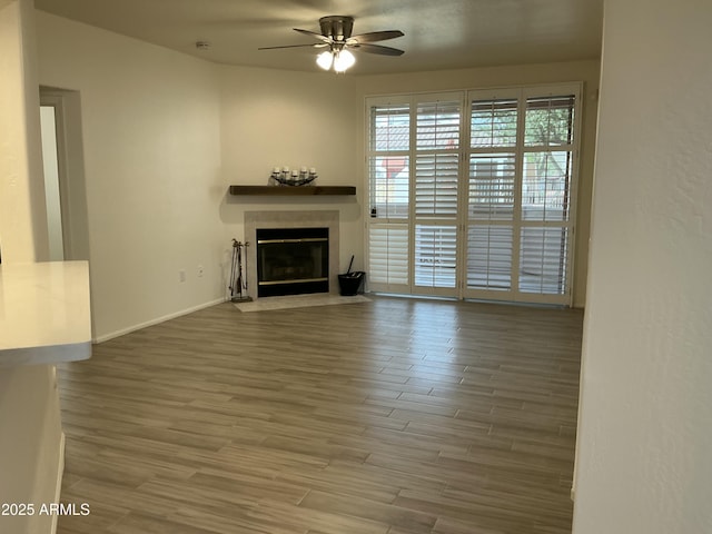 unfurnished living room with a fireplace with flush hearth, ceiling fan, wood finished floors, and baseboards