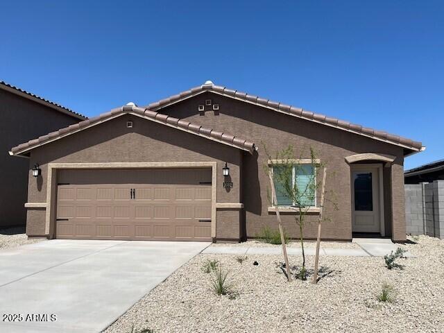 ranch-style house featuring concrete driveway, a tiled roof, an attached garage, and stucco siding