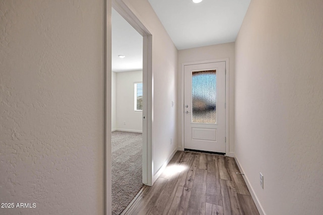 doorway with light wood-style floors, a textured wall, and baseboards