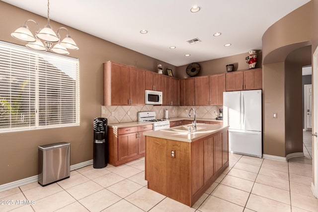 kitchen featuring tasteful backsplash, an island with sink, sink, hanging light fixtures, and white appliances