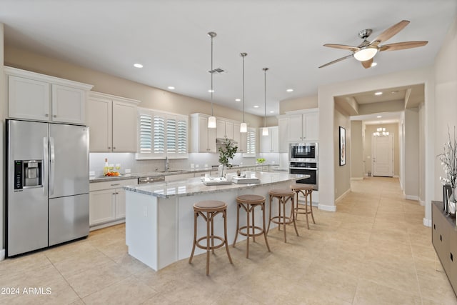 kitchen with appliances with stainless steel finishes, sink, white cabinets, a center island, and light stone countertops