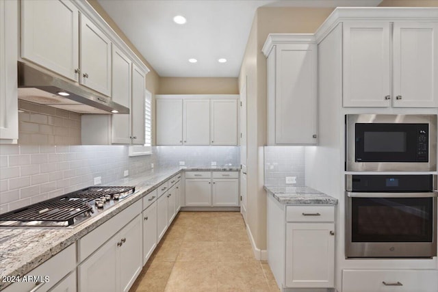 kitchen with white cabinets, light tile patterned floors, tasteful backsplash, appliances with stainless steel finishes, and light stone countertops