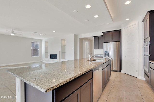 kitchen featuring sink, light stone counters, light tile patterned floors, appliances with stainless steel finishes, and a kitchen island with sink