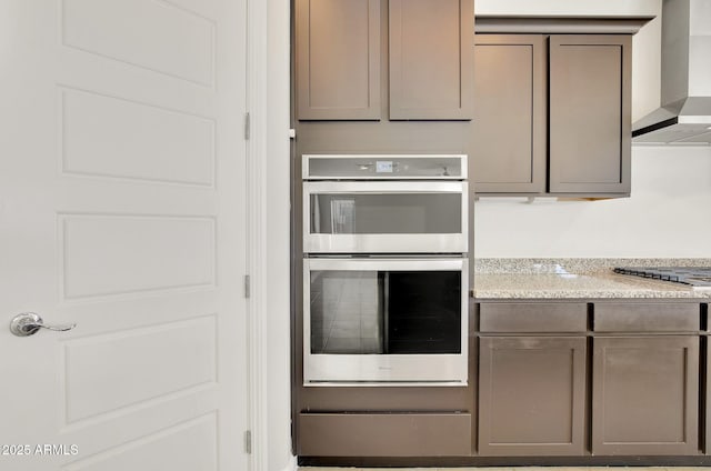 kitchen featuring gas cooktop, stainless steel double oven, light stone countertops, and wall chimney range hood