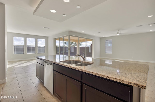 kitchen with sink, a kitchen island with sink, stainless steel dishwasher, light tile patterned floors, and light stone countertops