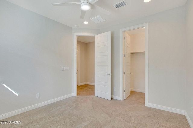 unfurnished bedroom with a walk in closet, light colored carpet, ceiling fan, and a closet