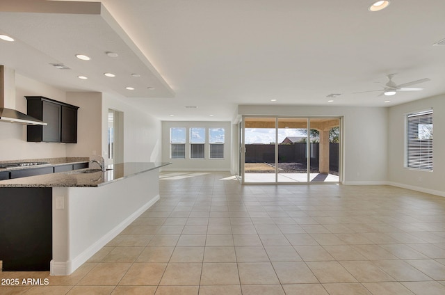 kitchen with stainless steel gas cooktop, wall chimney range hood, light tile patterned floors, and dark stone counters