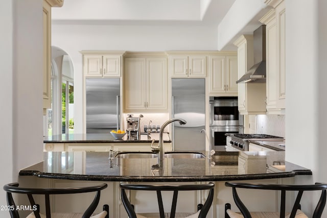 10754 E Laurel Ln, Scottsdale, AZ 85259 - kitchen featuring wall chimney exhaust hood, appliances with stainless steel finishes, tasteful backsplash, and dark stone countertops