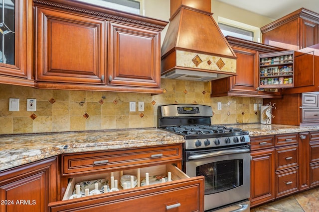 kitchen with backsplash, light stone countertops, stainless steel range with gas cooktop, and premium range hood