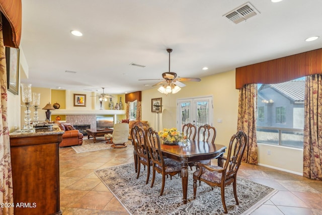 tiled dining area with ceiling fan, a tile fireplace, and french doors