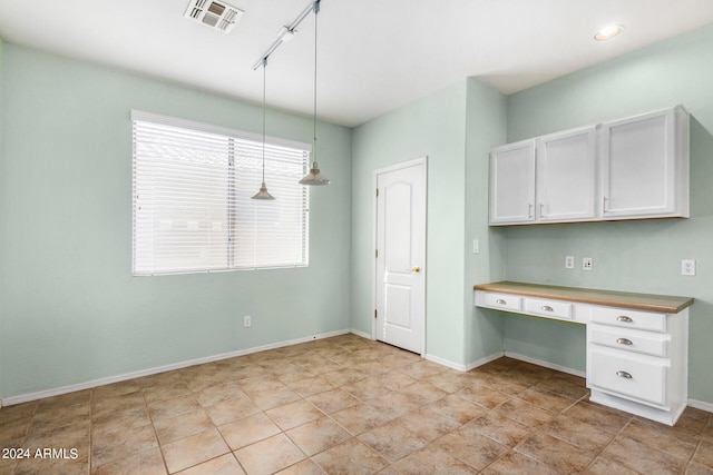 kitchen with built in desk, white cabinetry, track lighting, and pendant lighting