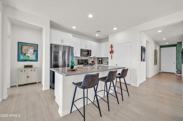 kitchen featuring white cabinetry, a breakfast bar area, decorative backsplash, a center island with sink, and appliances with stainless steel finishes