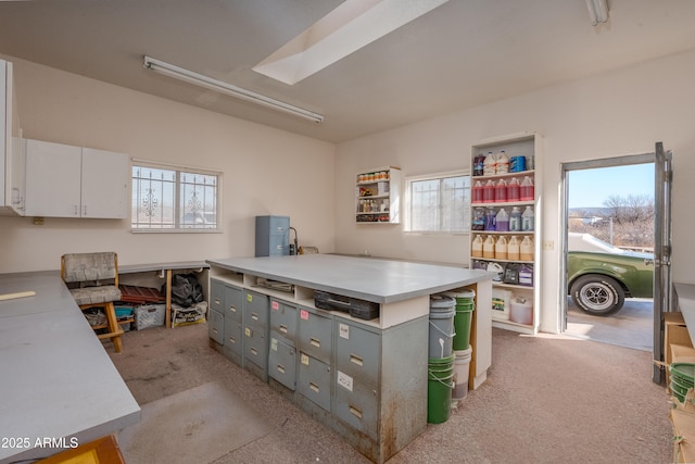 kitchen with a kitchen island, light colored carpet, light countertops, gray cabinets, and white cabinetry