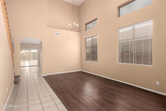 empty room with a towering ceiling, light wood-type flooring, and a notable chandelier