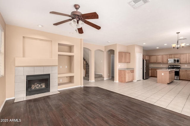 unfurnished living room featuring ceiling fan with notable chandelier, built in features, a tile fireplace, and light tile patterned flooring